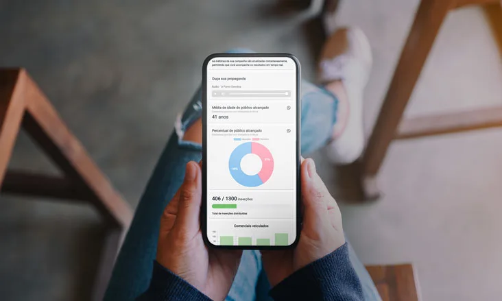 Mãos femininas segurando um celular virado para cima com a tela mostrando dados e gráficos de um relatório da interface do software Metrics
